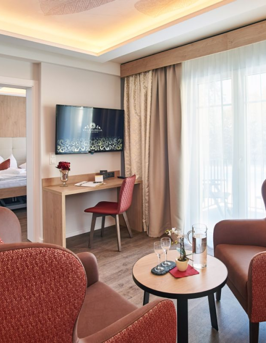 Modern eingerichtetes Einzelzimmer mit Bett, Sessel, Tisch und großem Fenster.